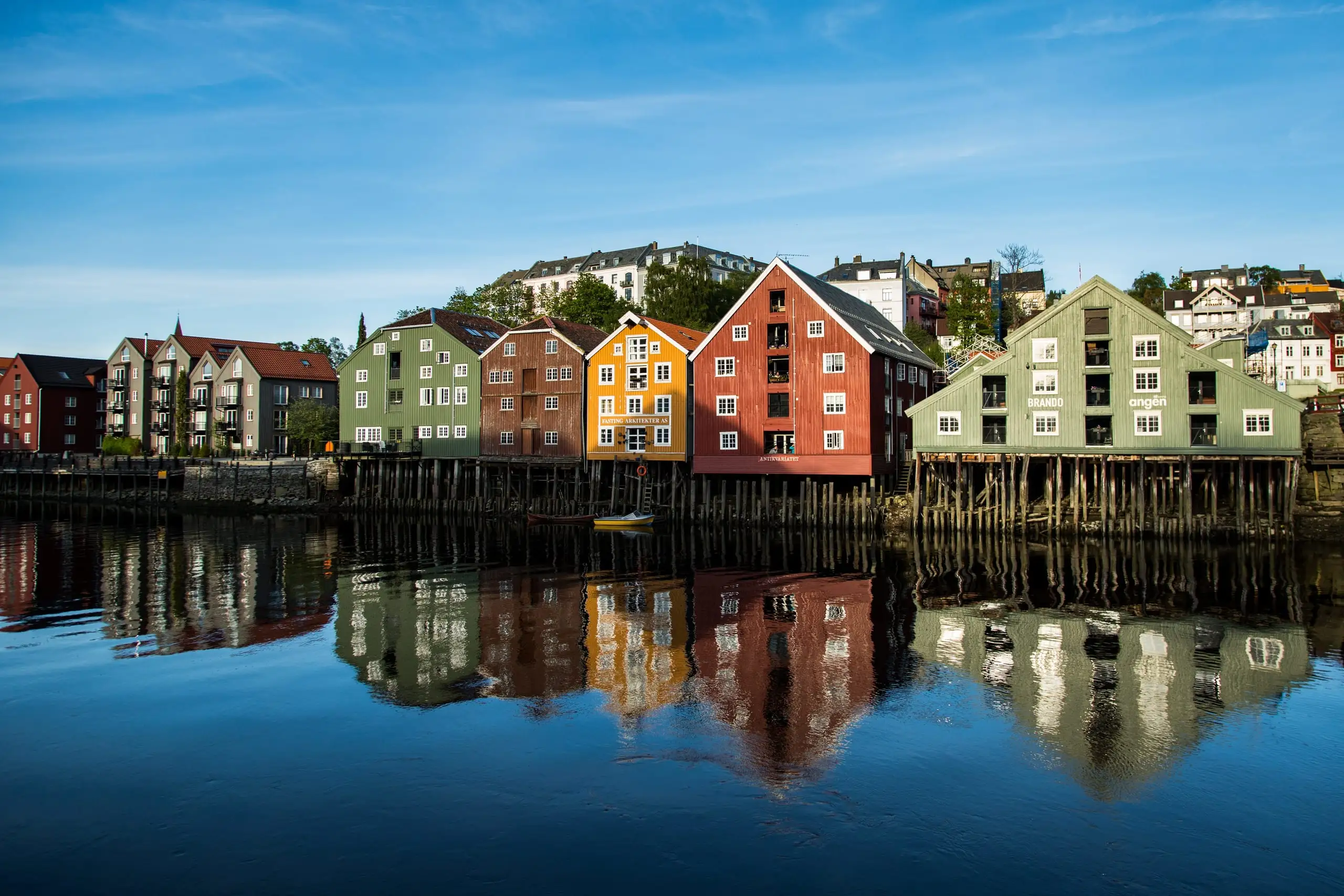 Bunte Speicherhäuser auf Stelzen am Flussufer, im Wasser gespiegelt unter blauem Himmel